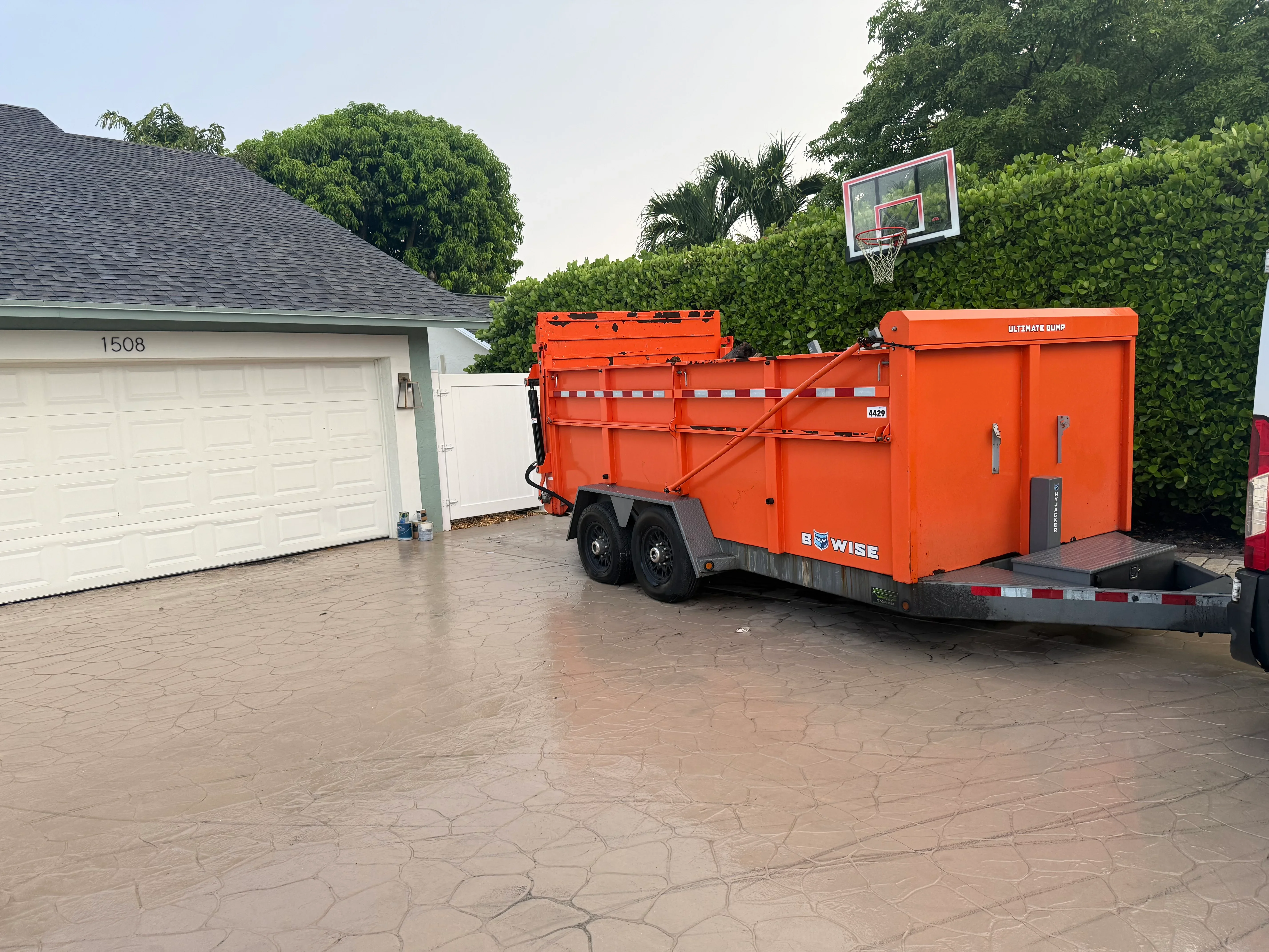 Orange dump trailer with hydraulic bed and safety chains on residential driveway