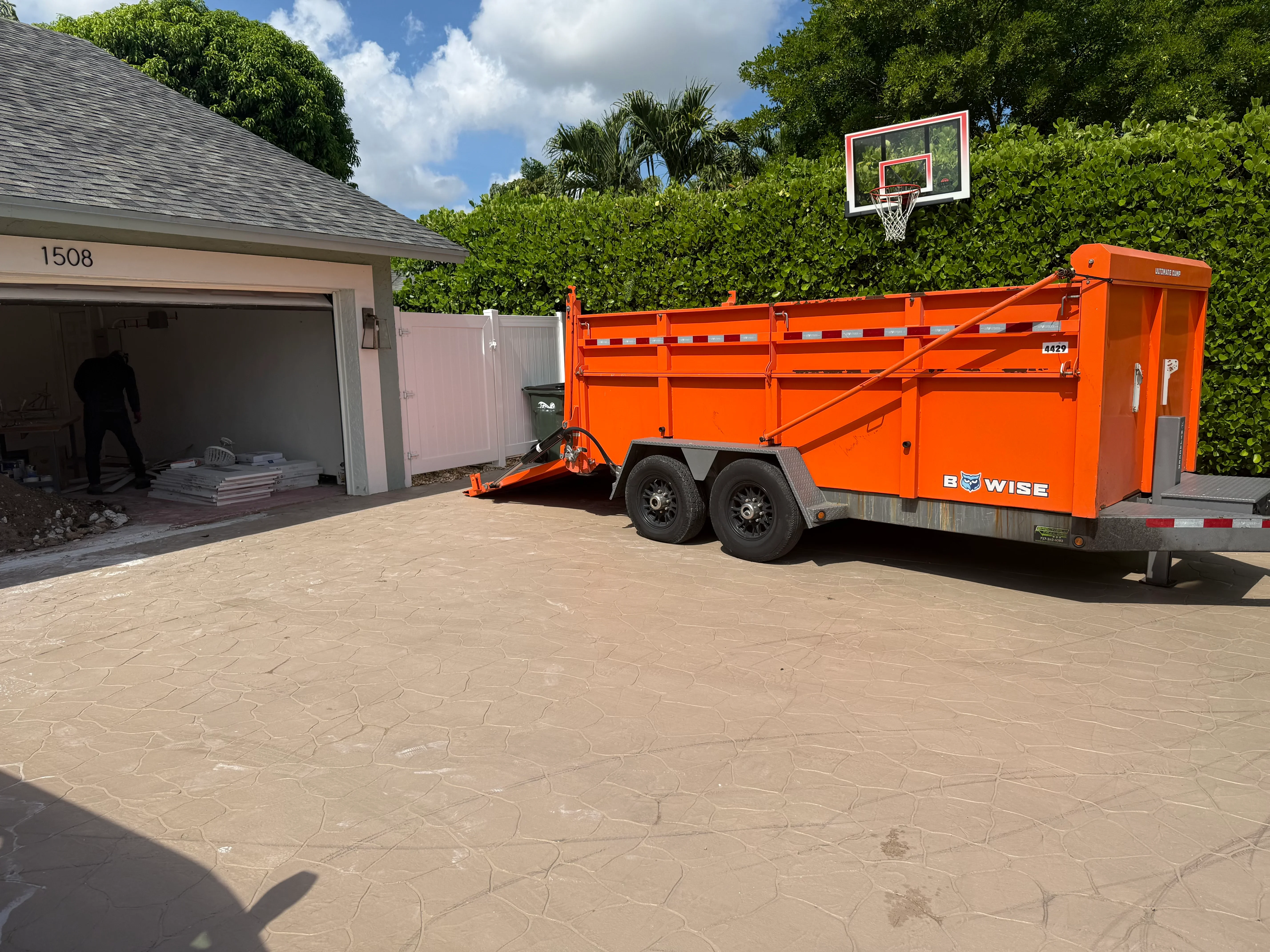 Orange dump trailer positioned at residential driveway for debris hauling and junk removal