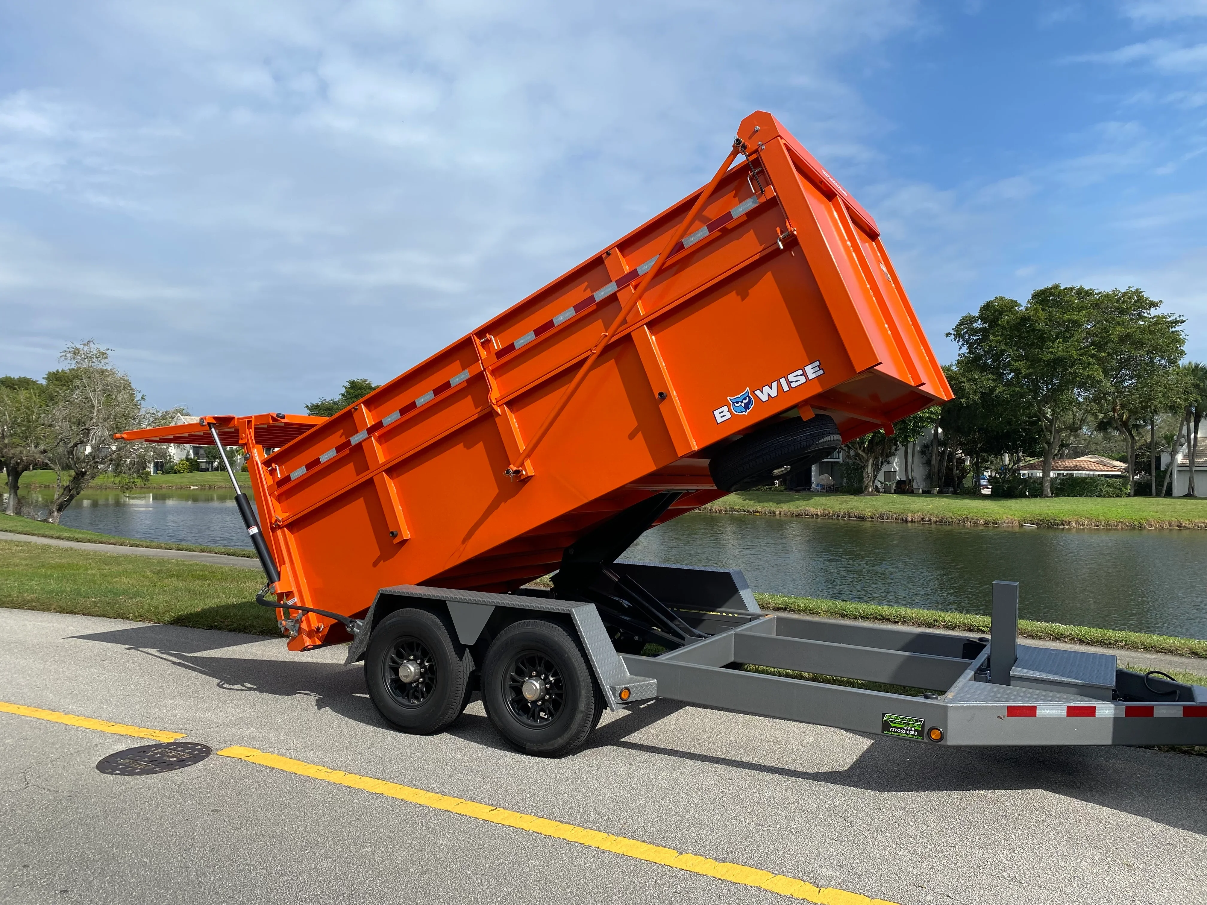 Orange dual-axle dump trailer with hydraulic lift system raised at full angle