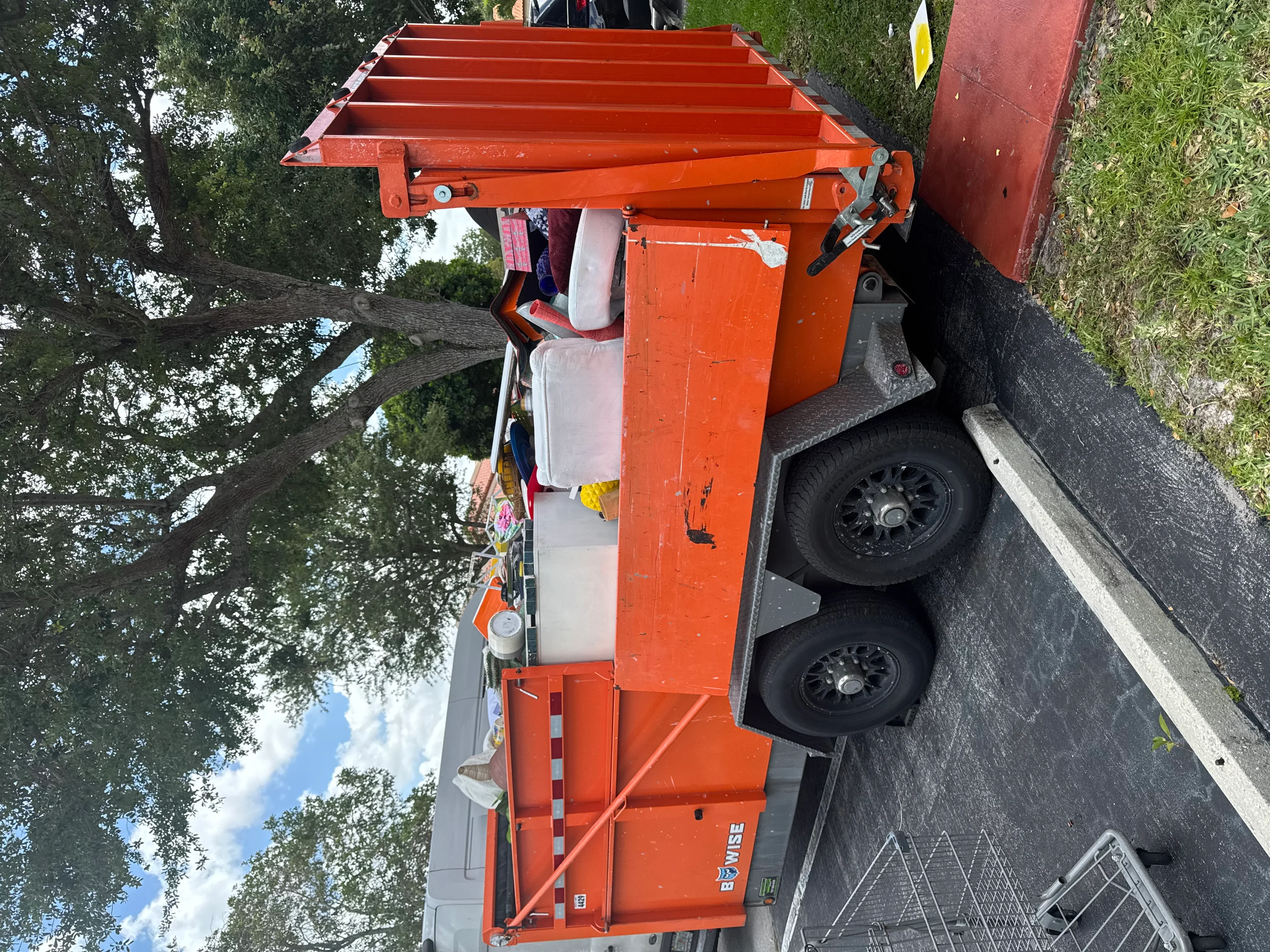 Orange hydraulic dump trailer with dual axles and tarp cover system