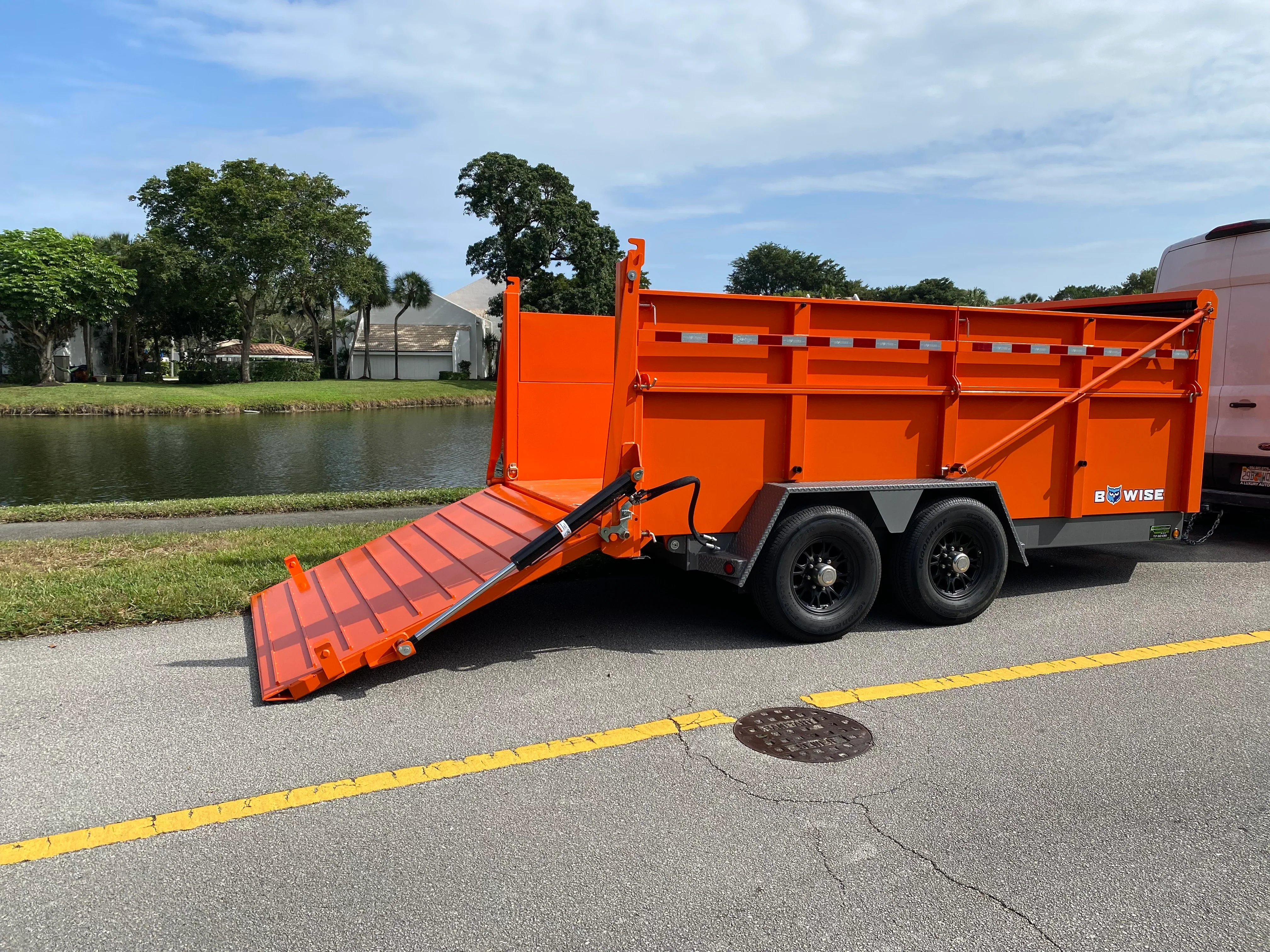 Orange dual-axle dump trailer with lowered ramp and hydraulic lift gate